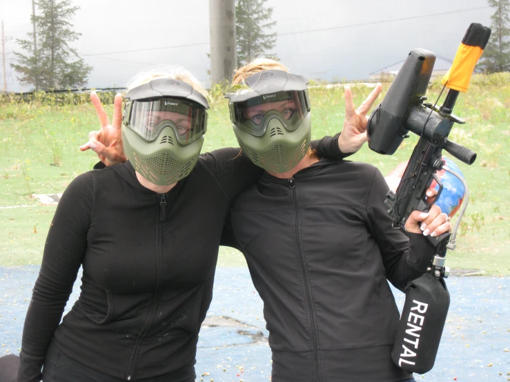 two woman with goggles, one holding a weapon and the other wearing a gas mask