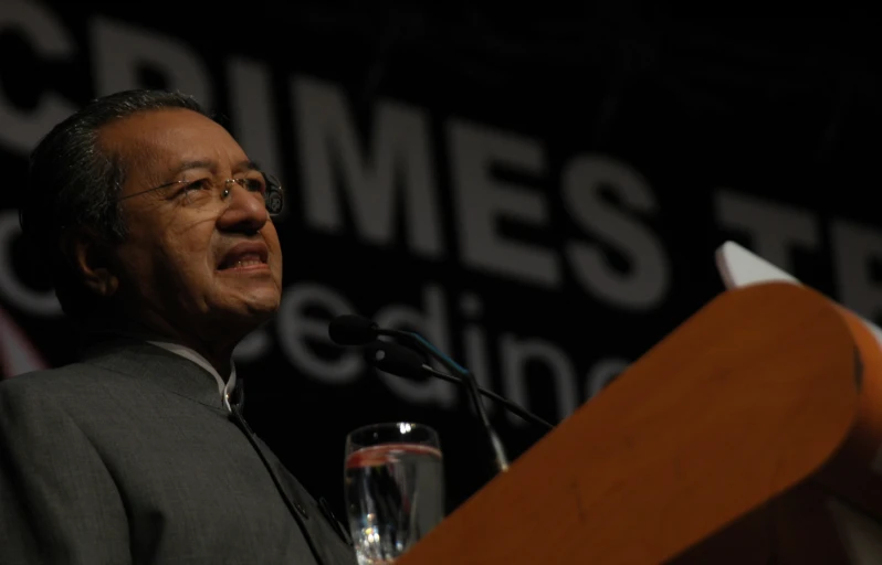 a man in glasses and suit stands at a podium