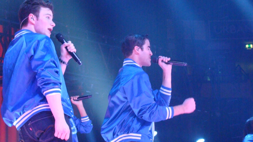 two young men wearing blue jackets singing into microphones