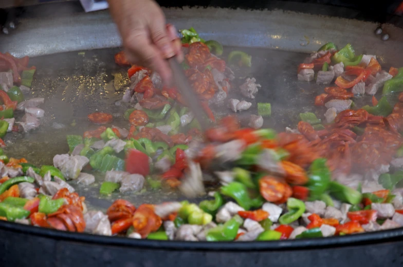 a wok that has soing that looks like peppers being stirred with a spatula