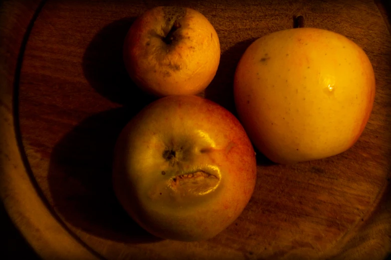 three apples and one orange sit on a wooden tray