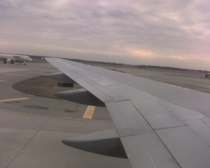 an airplane wing over a runway as it sits below a cloudy sky