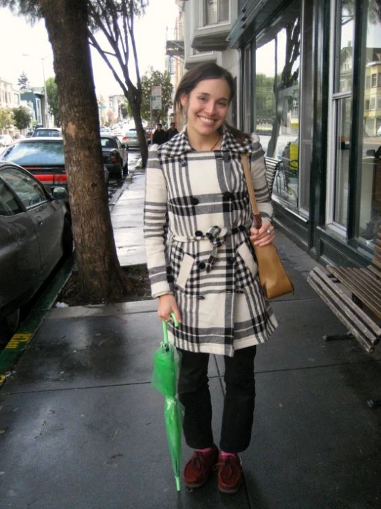 a woman in a dress and hat stands on a street corner