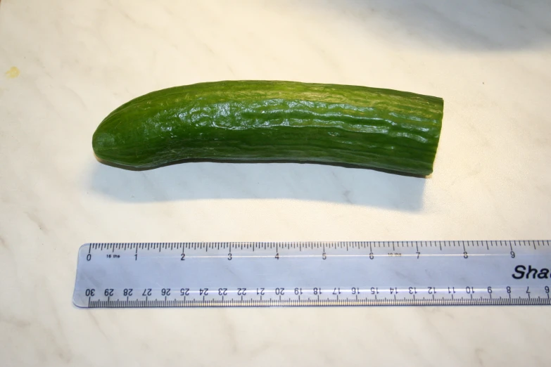 a cucumber and a measuring tape sit next to a knife