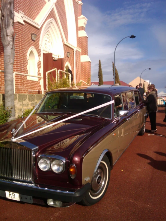 the large maroon rolls royce limousine is parked near a red brick building