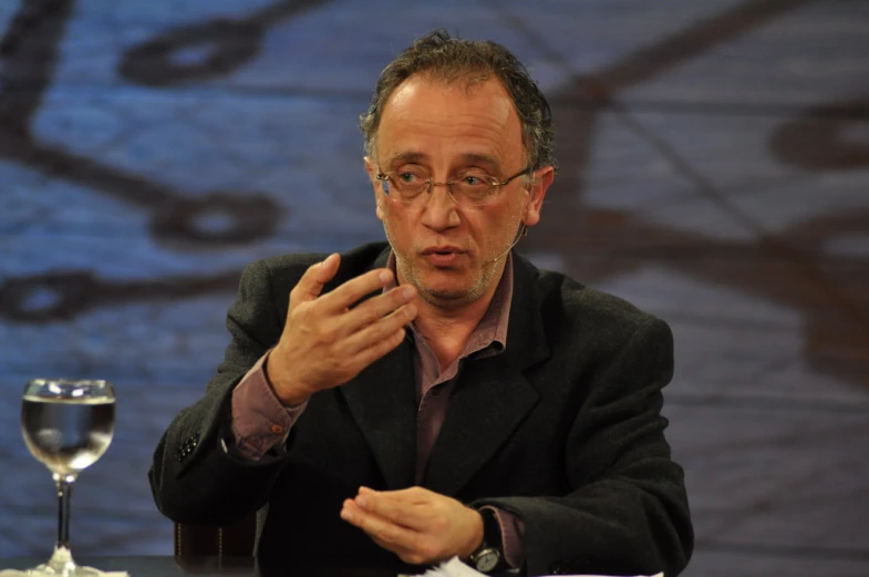 a man in a suit sits at a table and talks