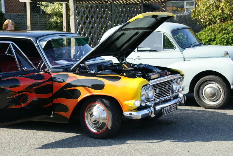 two vintage cars sitting side by side and the front has a flame paint job on it