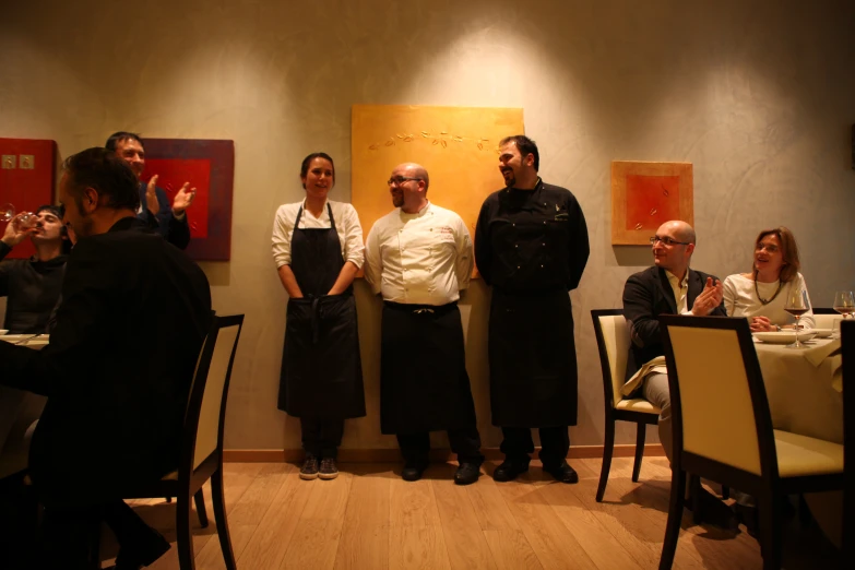 five chefs stand in a circle in front of two dining tables