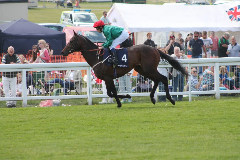 a jockey and horse running on grass near fence