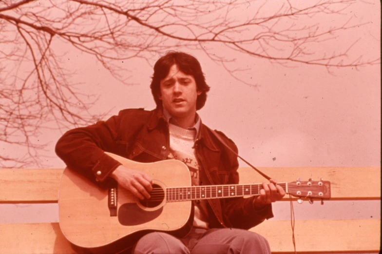 a young man holding an acoustic guitar on a bench