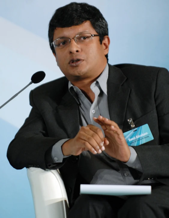 a man wearing glasses at a table speaking on stage