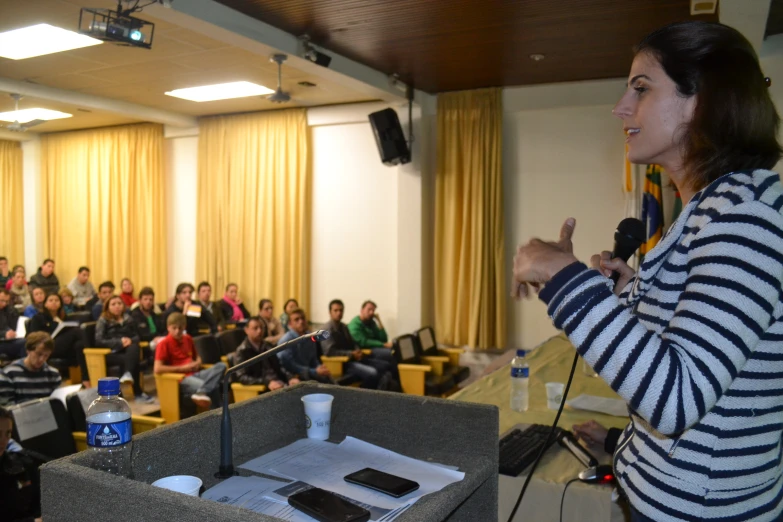 a woman standing at the microphone in front of a room full of people