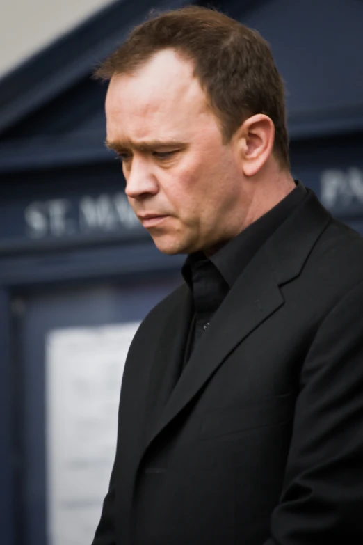 a man in a black suit standing with his hand in his pocket