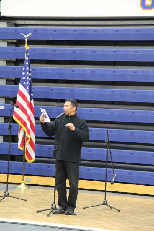 the man is speaking at the microphone near a flag