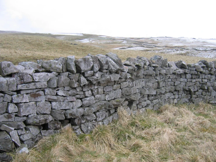 there is a fence built out of rocks that are in the grass