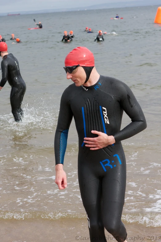 two swimmers in full wetsuits walking on the beach