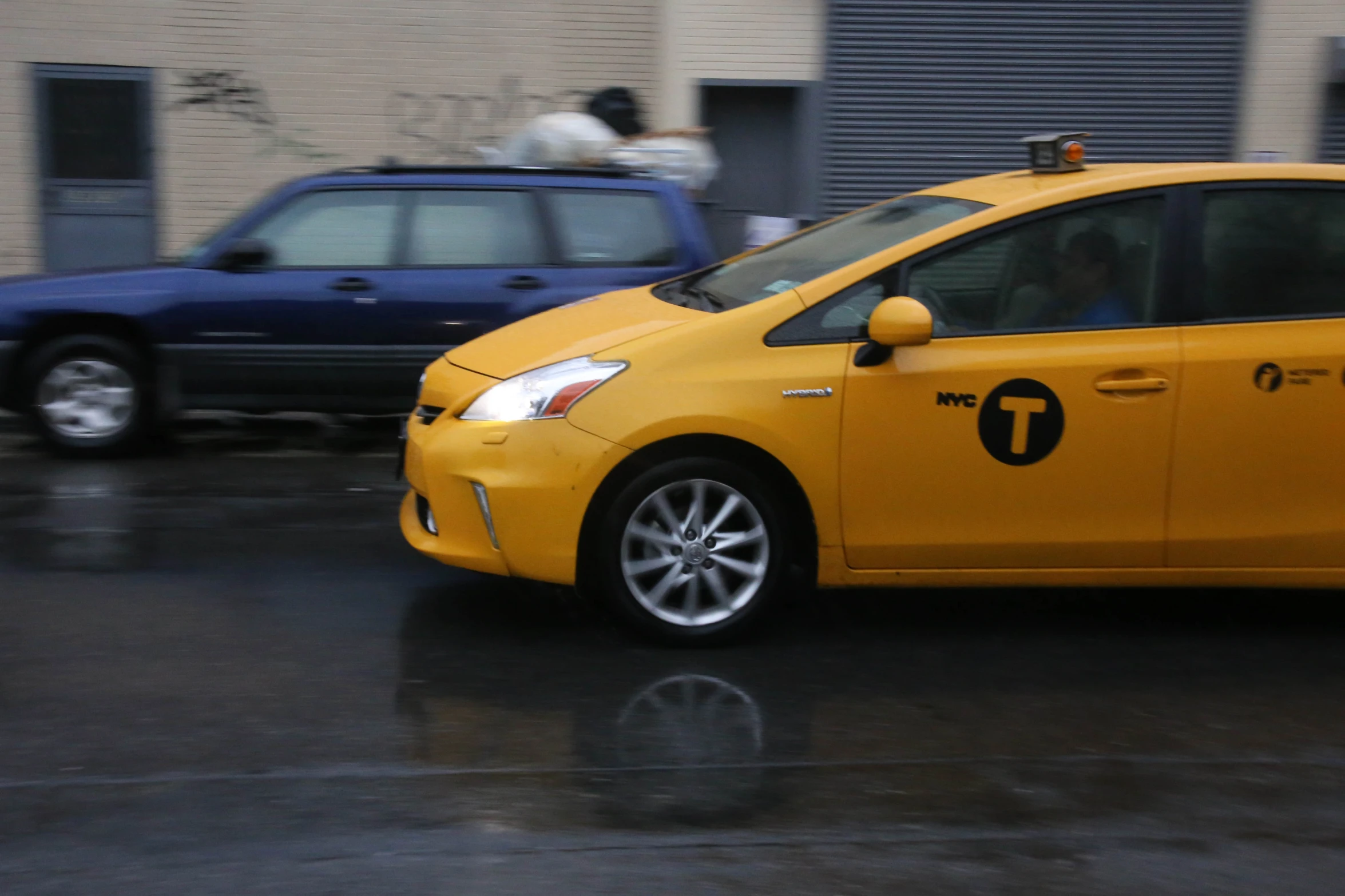 a yellow taxi driving down a street next to a blue car