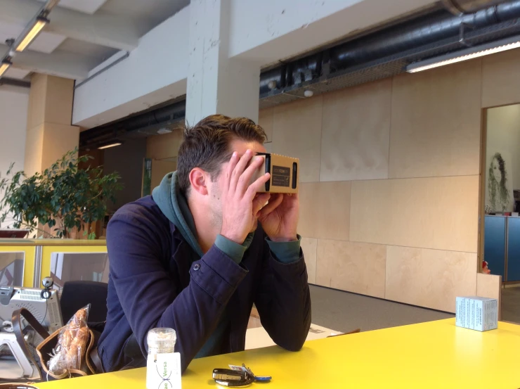 man in an office setting holding up his camera to his face