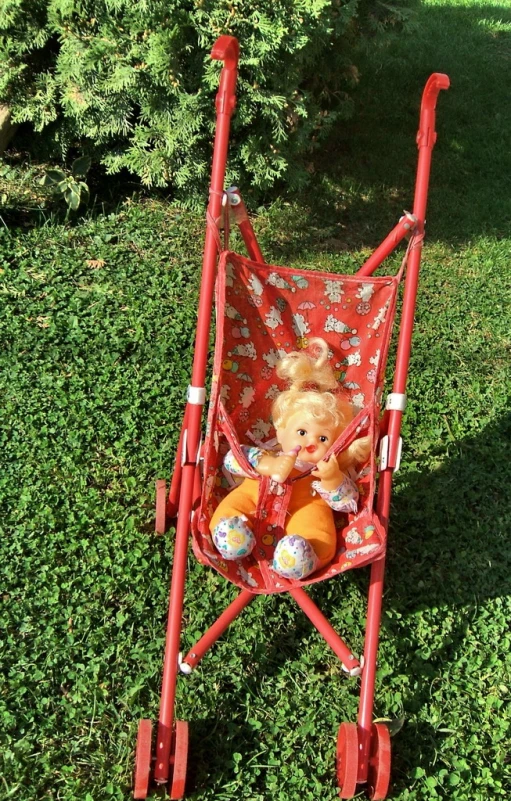 a small teddy bear in a toy stroller in the grass