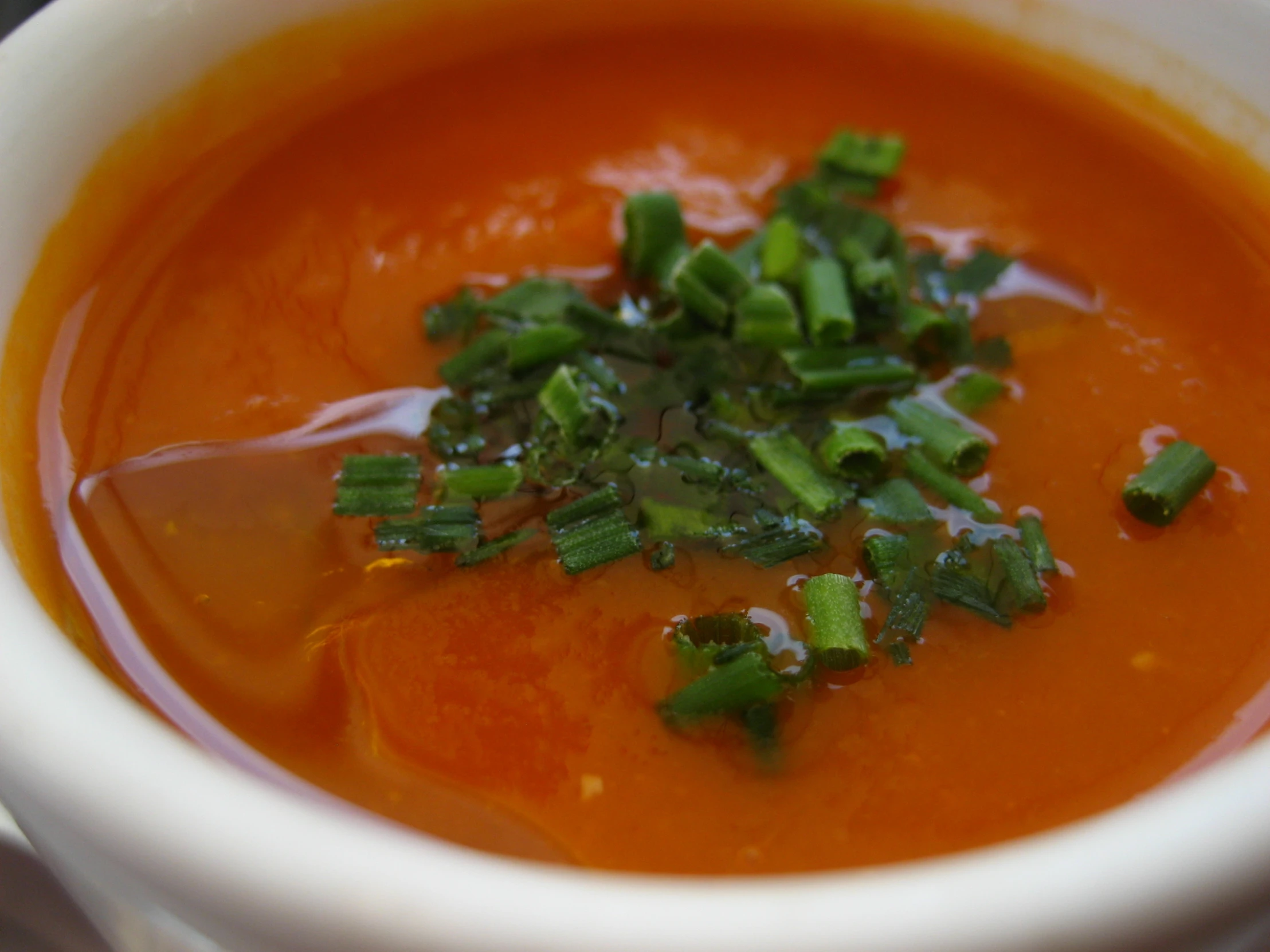 a white bowl filled with soup with chopped green onion on top