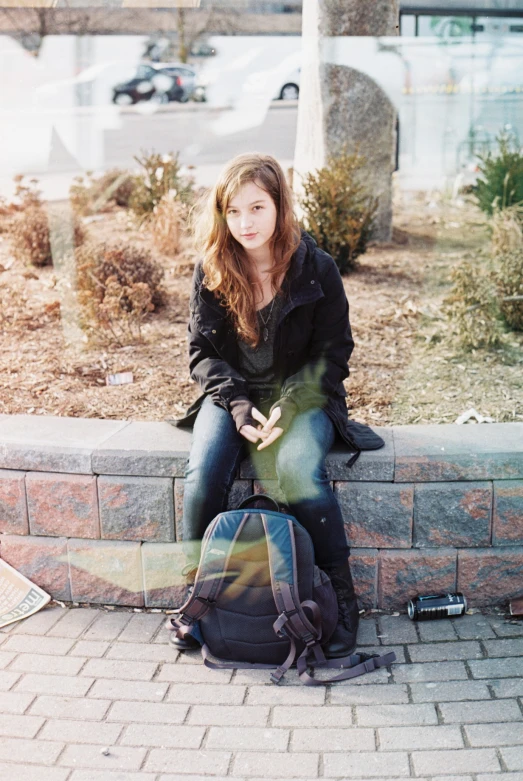 a girl sitting on top of a brick wall next to a backpack