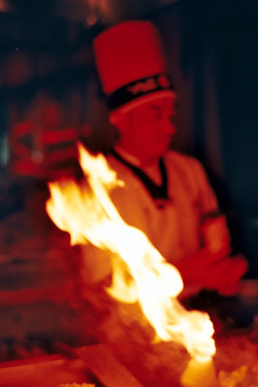 a chef roasting sausages with flames on an open fire pit