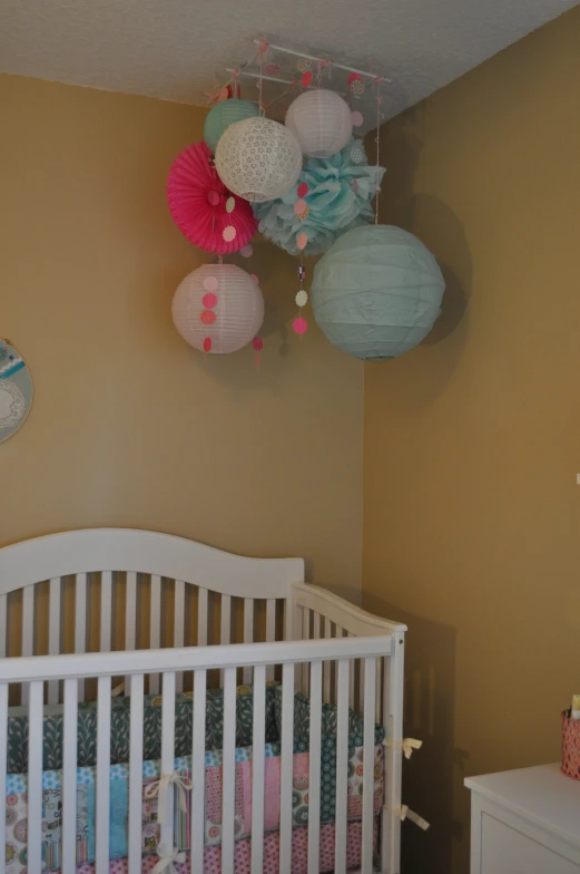 a white crib sits under some hanging paper lantern decorations