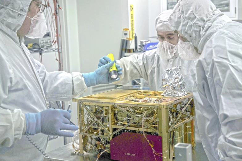 three men in white lab coats inspecting a small structure