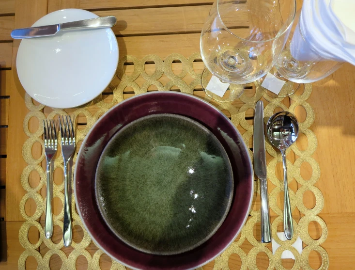 a bowl on a place mat with silverware and glass