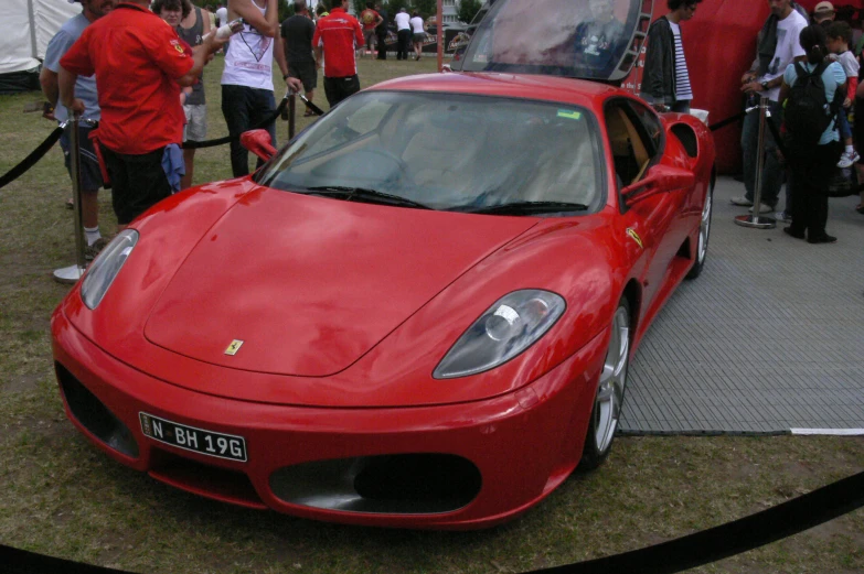 a ferrari sits parked on the side of a road while people are milling around it