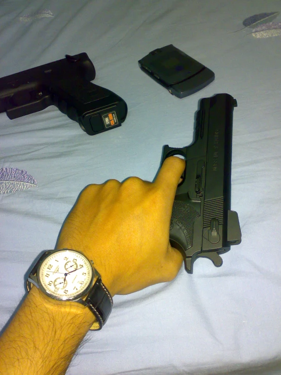 a man's arm holds a gun, watch and smart phone