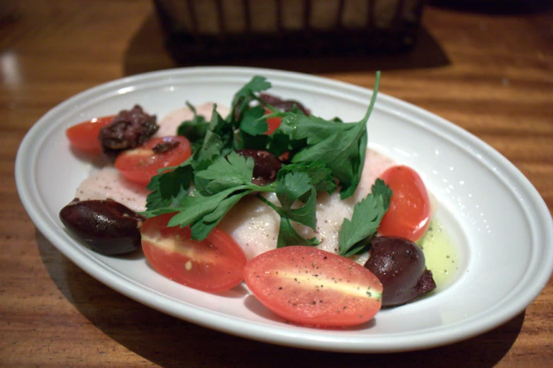 a white plate has tomatoes and olives with greens