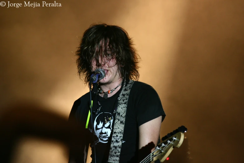 a man with heavy hair playing guitar in a microphone