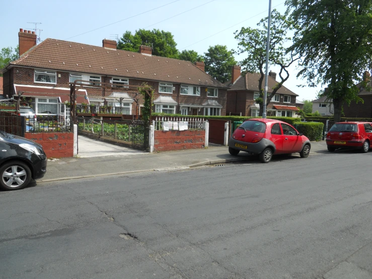 a residential street with small cars parked and two brick houses in the background