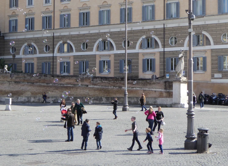 children play with bubbles on a square in front of a huge building