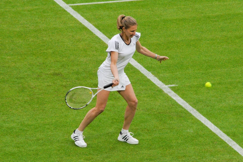 a woman in a white dress playing tennis on grass