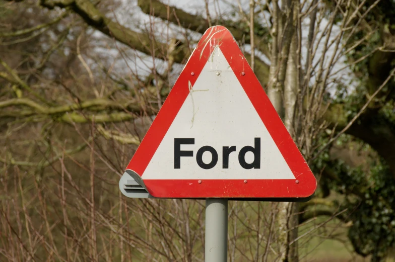 a red and white triangle sign in front of trees