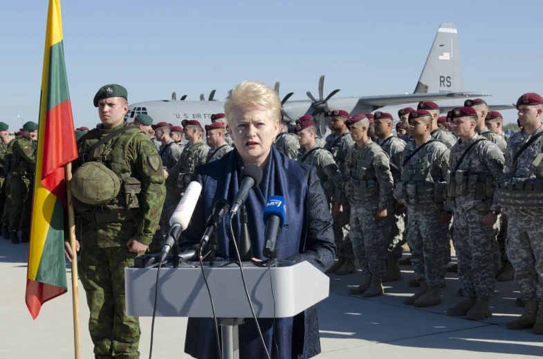 a woman wearing a blue jacket is speaking in front of soldiers