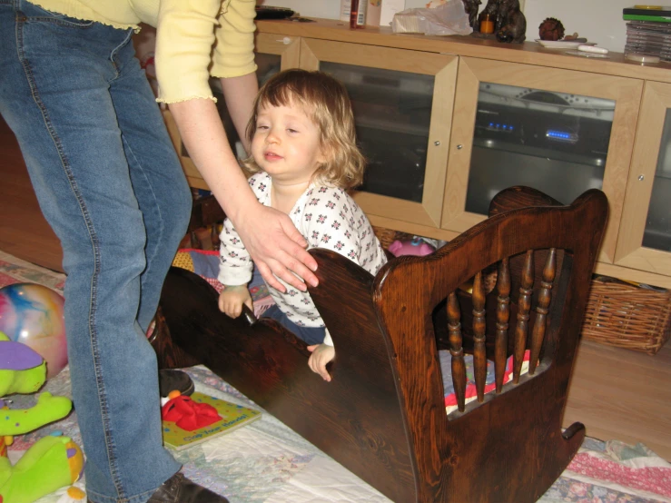 woman helping small child climb in wooden toddler bed