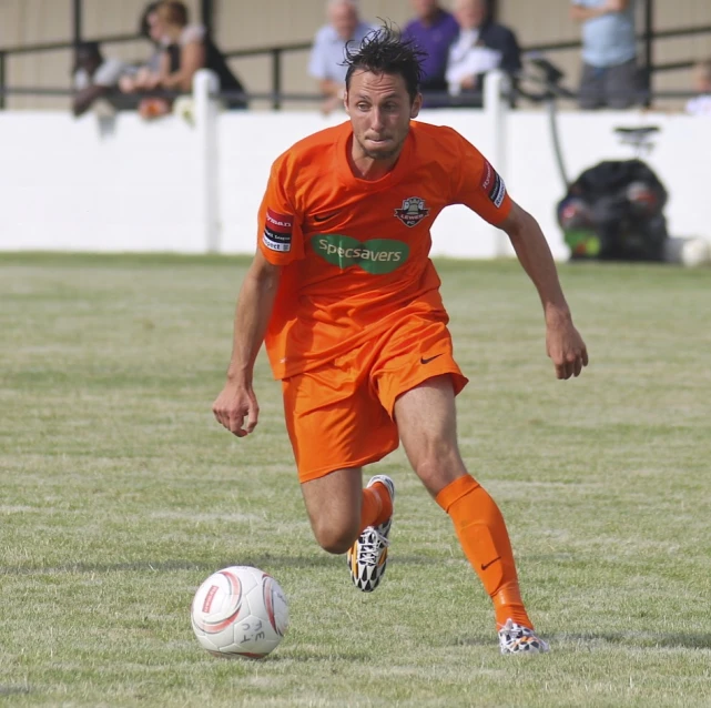 a man in an orange uniform is running towards a soccer ball