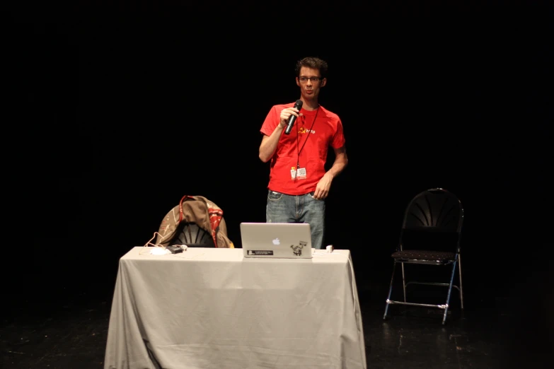 a young man standing at a table holding a microphone