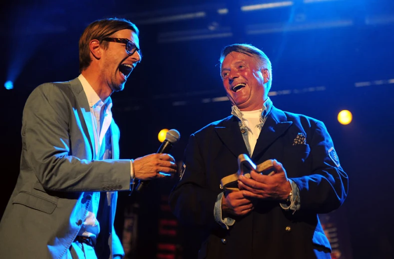 two men are standing talking and holding microphones