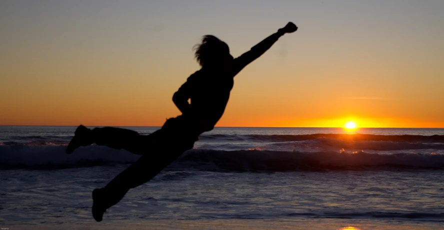 a person leaping into the air over water at sunset