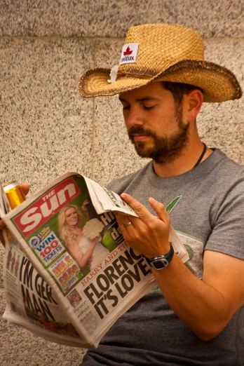 a man wearing a straw hat holding a  dog and reading a newspaper