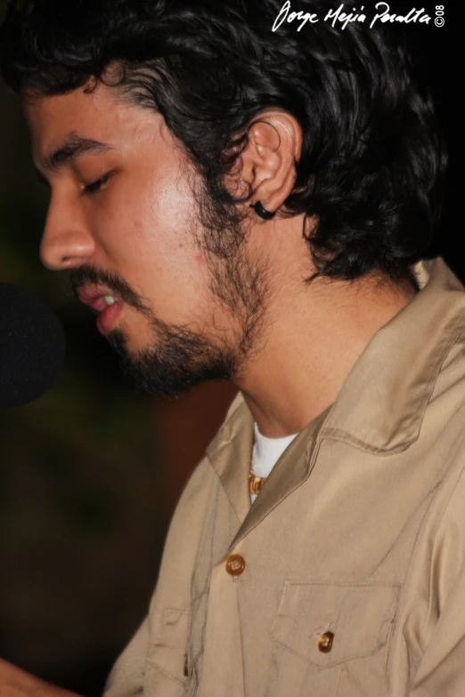a man with a beard wearing earrings while holding a microphone