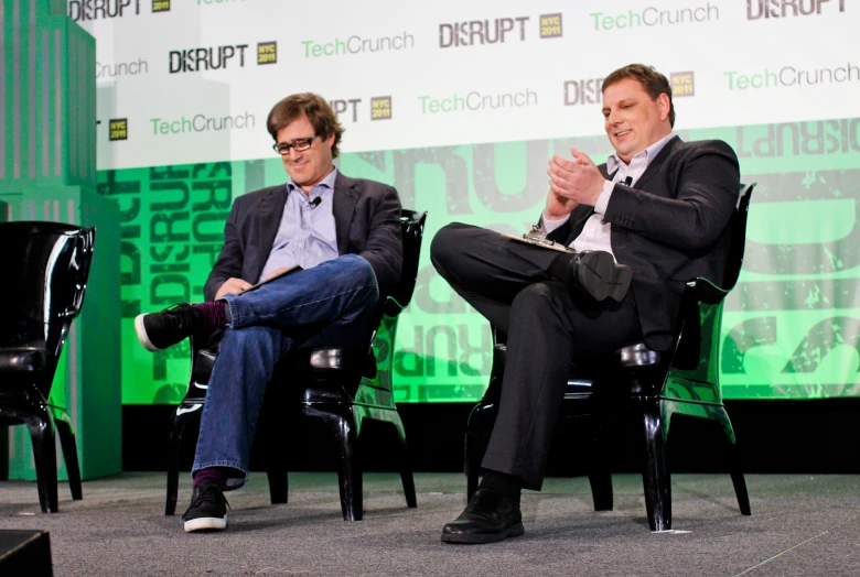 two men sitting in chairs facing opposite directions while having their feet crossed