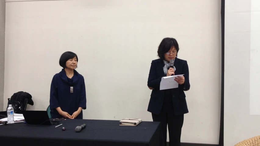 two women stand at a table with microphones