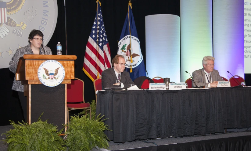 a man standing at a podium near two others in front of flags