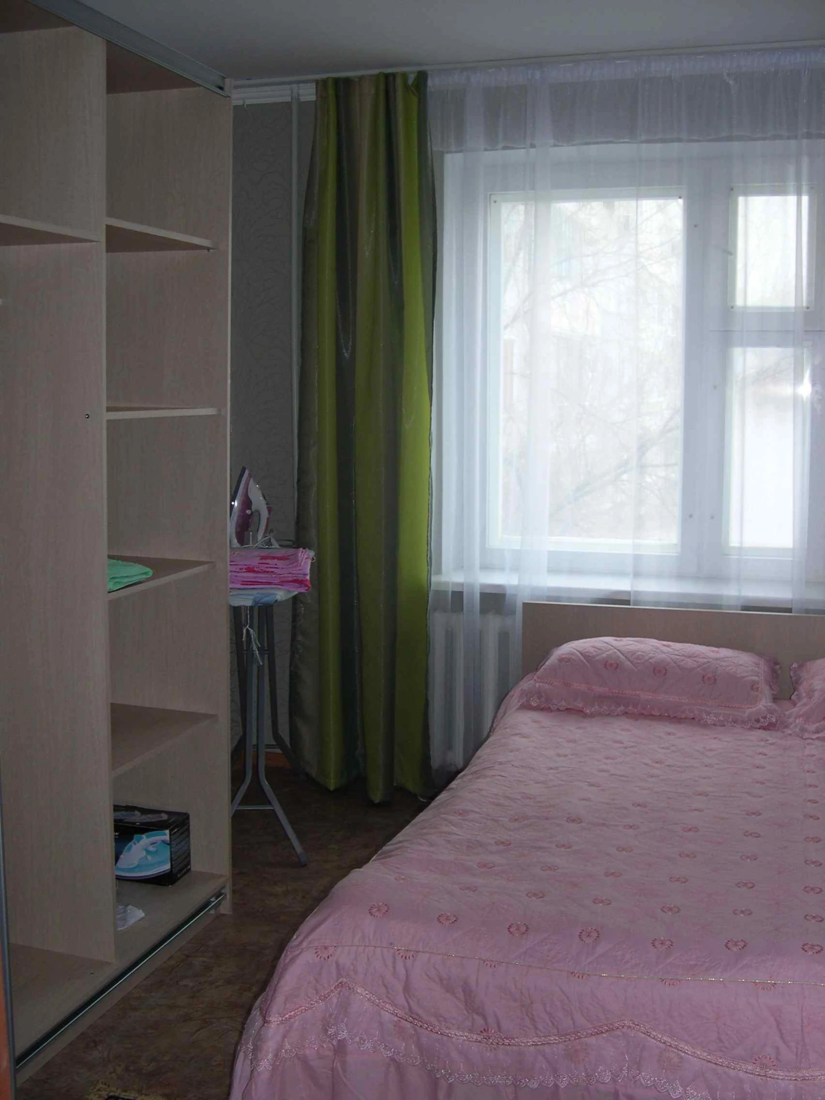 a room with a bed, bookcase and large windows