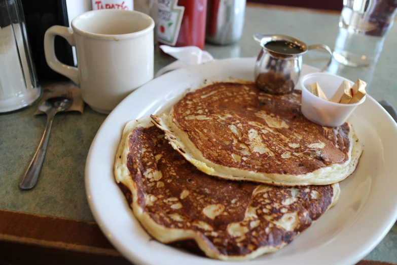 two pancakes stacked on a plate next to a cup of coffee